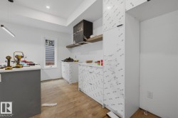 Modern kitchen space featuring recessed lighting, a linear pendant fixture, wood-finish flooring, a contemporary range hood with an integrated shelf, and white cabinetry - 