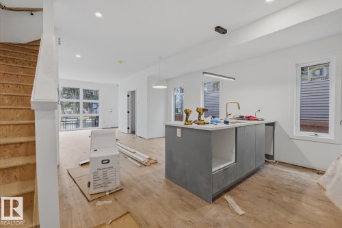 Open-concept living space with wood-finish flooring, recessed lighting, and a kitchen island featuring a gold-finish faucet - 11327 122 Street, Edmonton, AB - Indoor