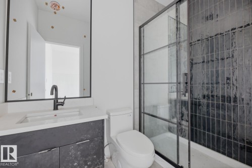Modern bathroom featuring a dark framed mirror, white countertop vanity with dark cabinetry, and a black framed glass shower enclosure with dark vertical tile - 11327 122 Street, Edmonton, AB - Indoor Photo Showing Bathroom