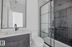 Modern bathroom featuring a dark framed mirror, white countertop vanity with dark cabinetry, and a black framed glass shower enclosure with dark vertical tile - 