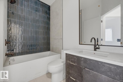 Bathroom featuring a vanity with an integrated sink and light-toned countertop, a rectangular mirror, and a bathtub with full-height subway tile surround - 11327 122 Street, Edmonton, AB - Indoor Photo Showing Bathroom