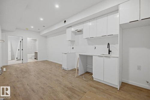 Contemporary kitchen area featuring white flat-panel cabinetry, a white countertop, and a matte black single-handle faucet over an undermount sink - 11327 122 Street, Edmonton, AB - Indoor Photo Showing Other Room