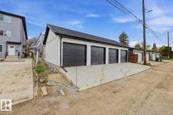 Multi-unit garage structure featuring four dark paneled garage doors, white siding, black trim, and a dark shingle roof - 