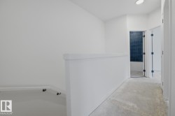 Hallway featuring a partial staircase, recessed lighting, and a doorway with dark blue subway tile - 