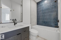Bathroom featuring a dark blue vertical tile shower surround, matte black fixtures, a white soaking tub, and a vanity with a white countertop and integrated sink - 