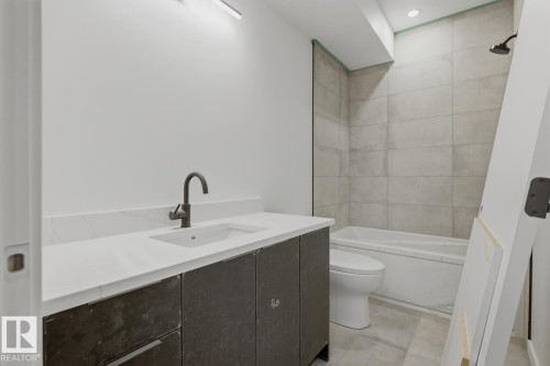 Modern bathroom featuring a dark grey vanity with a white countertop and integrated sink, a matte black faucet, and a bathtub with light grey wall tiling - 11327 122 Street, Edmonton, AB - Indoor Photo Showing Bathroom