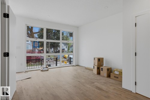 Expansive multi-pane window system, light wood-finish flooring, recessed ceiling lighting, crisp white walls, and a white interior door with black hardware - 11327 122 Street, Edmonton, AB - Indoor