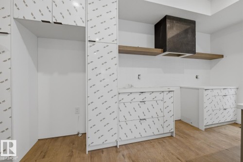 Contemporary kitchen space featuring wood-finish flooring, white cabinetry with protective film, and an integrated hood vent - 11327 122 Street, Edmonton, AB - Indoor Photo Showing Other Room