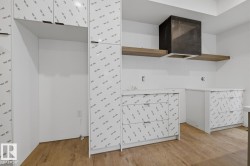 Contemporary kitchen space featuring wood-finish flooring, white cabinetry with protective film, and an integrated hood vent - 