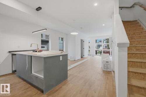 Open-concept living space with wood-finish flooring, recessed lighting, and a contemporary kitchen island featuring a light-colored countertop and a gold-tone faucet - 11327 122 Street, Edmonton, AB - Indoor