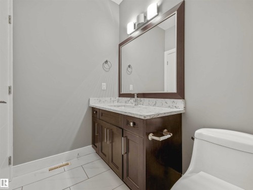 Bathroom featuring a dark wood-finish vanity with a light-toned countertop, a rectangular mirror, and a three-bulb vanity light fixture - 1090 Armitage Crescent, Edmonton, AB 