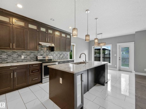 Modern kitchen featuring dark wood-finish cabinetry, stainless steel appliances, and a mosaic tile backsplash - 1090 Armitage Crescent, Edmonton, AB 