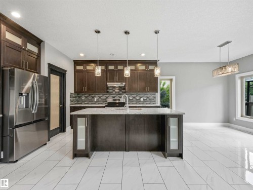 Spacious kitchen featuring dark wood cabinetry, a large kitchen island with a stone-finish countertop, a stainless steel French door refrigerator, and a tile backsplash - 1090 Armitage Crescent, Edmonton, AB 
