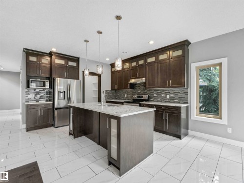 Kitchen featuring wood-finish cabinetry, stainless steel appliances, a center island with a stone countertop, and pendant lighting - 1090 Armitage Crescent, Edmonton, AB 