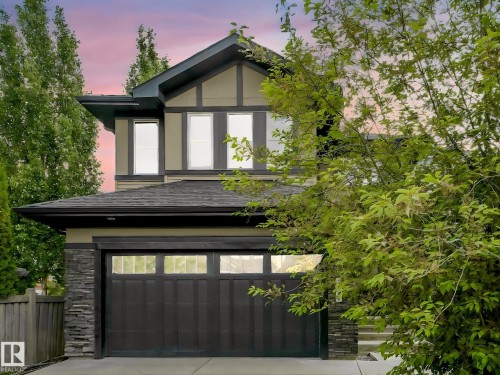 Modern exterior featuring a dark-toned garage door with horizontal glass panels, stone veneer accents, and a paved driveway - 1090 Armitage Crescent, Edmonton, AB 