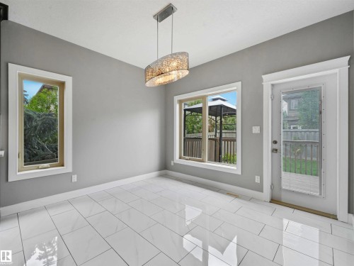 Bright interior space featuring large format white tile flooring, a contemporary chandelier, two windows with white trim, a glass-paned exterior door with white trim, and light gray wall paint - 1090 Armitage Crescent, Edmonton, AB 