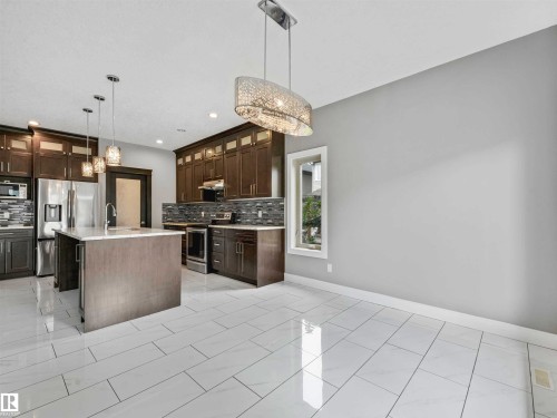 Modern kitchen featuring stainless steel appliances, dark wood cabinetry, a central island with a sink, and pendant lighting - 1090 Armitage Crescent, Edmonton, AB 