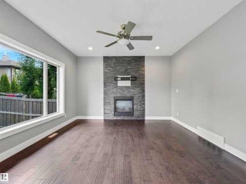 Living area featuring dark wood-finish flooring, light grey walls, and a recessed fireplace with a stone surround - 1090 Armitage Crescent, Edmonton, AB 