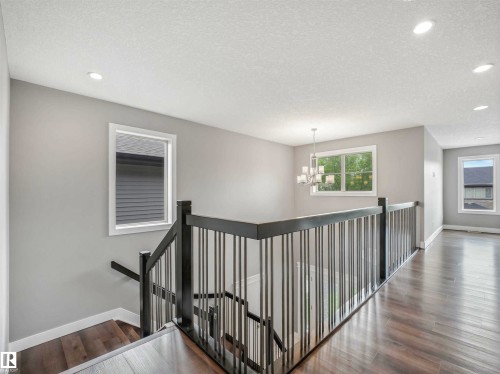 Upper-level landing featuring wood-finish flooring, contemporary chandelier, recessed lighting, and a dark wood-finish railing with vertical balusters - 1090 Armitage Crescent, Edmonton, AB 