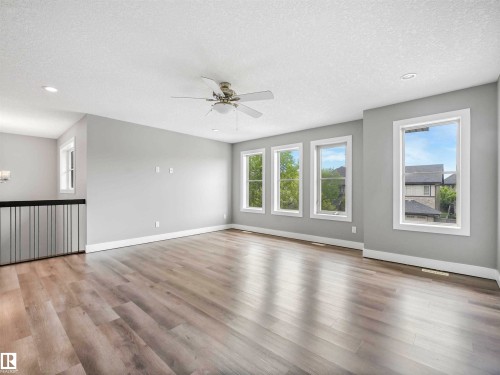 Spacious room featuring light wood-finish flooring, multiple large windows with white trim, and a ceiling fan with integrated lighting - 1090 Armitage Crescent, Edmonton, AB 