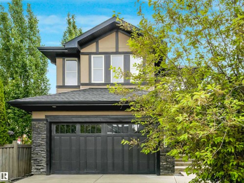Two-story residence featuring a dark gray garage door, stacked stone accents, and a contrasting tan and dark brown exterior - 1090 Armitage Crescent, Edmonton, AB 