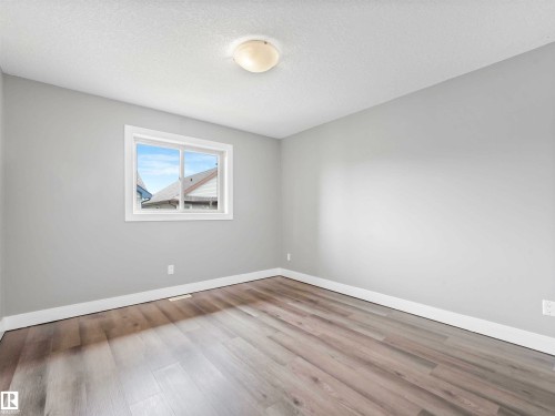 Bright interior space featuring light wood-finish flooring, neutral gray walls, white trim, and a window with white casing - 1090 Armitage Crescent, Edmonton, AB 