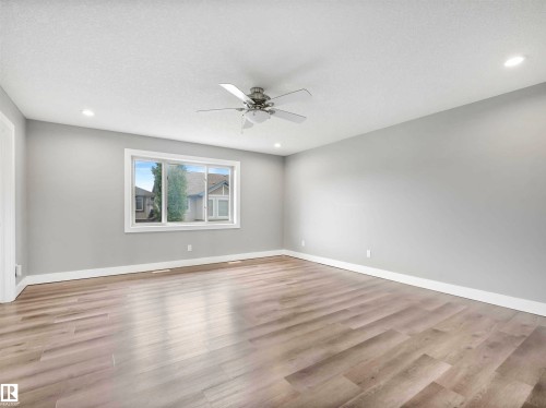 Spacious room featuring wood-finish flooring, light gray walls, a large window, recessed lighting, and a ceiling fan - 1090 Armitage Crescent, Edmonton, AB 
