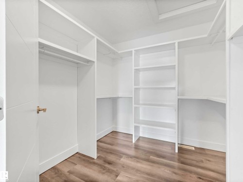 Spacious walk-in closet featuring custom shelving, hanging rods, light wood-finish flooring, and crisp white walls - 1090 Armitage Crescent, Edmonton, AB 