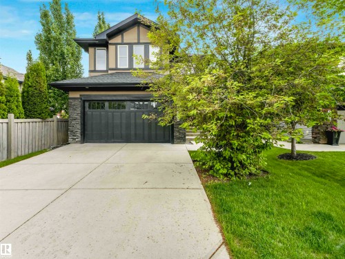 Two-story home with a dark gray garage door, light tan siding, dark trim accents, and stone veneer detailing - 1090 Armitage Crescent, Edmonton, AB 