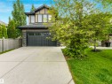 Two-story home with a dark gray garage door, light tan siding, dark trim accents, and stone veneer detailing - 1090 Armitage Crescent, Edmonton, AB 