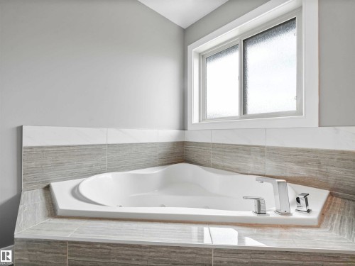 Corner soaking tub featuring a surrounding tiled deck, chrome fixtures, and a frosted window - 1090 Armitage Crescent, Edmonton, AB 