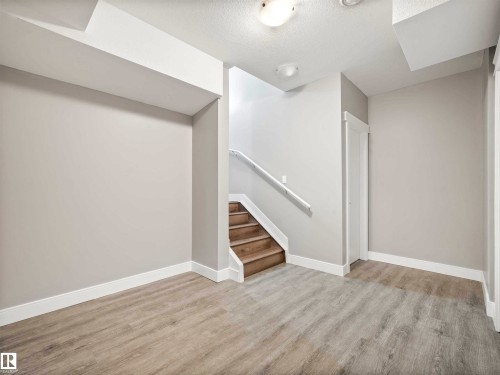 Open room featuring light wood-finish flooring and a staircase with a white railing - 1090 Armitage Crescent, Edmonton, AB 
