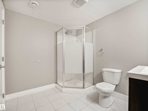 Three-piece bathroom featuring a corner glass shower enclosure, white toilet, and a vanity with a white countertop - 1090 Armitage Crescent, Edmonton, AB 