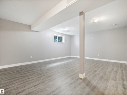 Spacious room featuring light-toned wood-finish flooring, crisp white baseboards, and a neutral wall color - 1090 Armitage Crescent, Edmonton, AB 