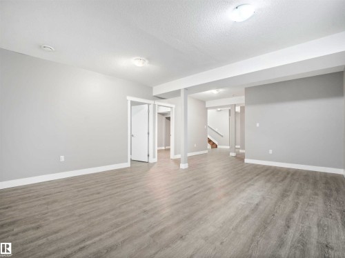 Spacious open-concept room featuring light gray wood-finish flooring, neutral gray walls, and white trim - 1090 Armitage Crescent, Edmonton, AB 