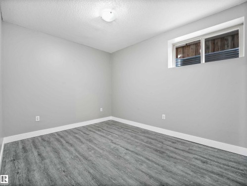 Bright room featuring light gray walls, wood-finish flooring, white baseboards, and a window with a corrugated metal window well - 1090 Armitage Crescent, Edmonton, AB 
