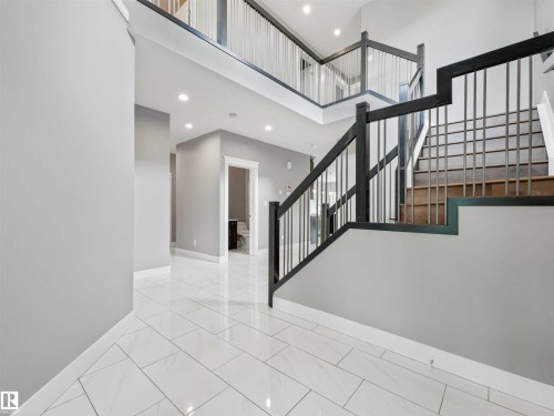 Two-story foyer featuring white tile flooring, a two-tone staircase with wood treads and metal balusters, and recessed ceiling lighting - 1090 Armitage Crescent, Edmonton, AB 