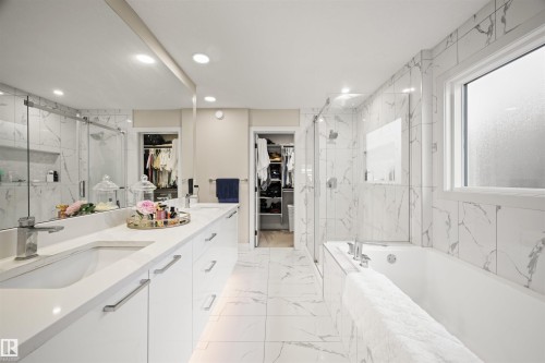 Contemporary bathroom featuring a built-in tub, separate glass-enclosed shower, dual vanity with undermount sinks, large wall-mounted mirror, and white marble-look tile flooring and walls - 12171 177 Avenue, Edmonton, AB 
