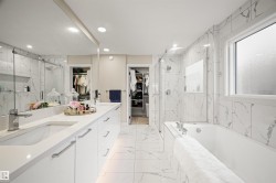 Contemporary bathroom featuring a built-in tub, separate glass-enclosed shower, dual vanity with undermount sinks, large wall-mounted mirror, and white marble-look tile flooring and walls - 