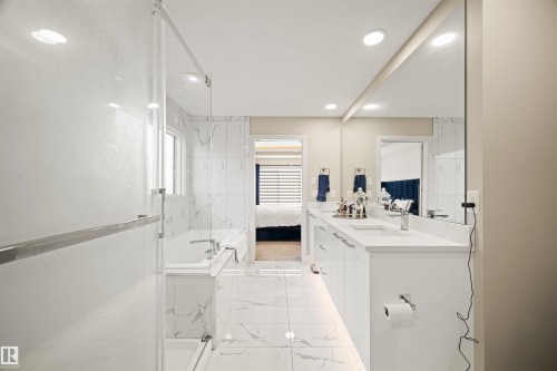 Contemporary bathroom featuring a double vanity with integrated sinks, a large wall-mounted mirror, recessed lighting, and a glass-enclosed shower with a separate soaking tub - 12171 177 Avenue, Edmonton, AB 