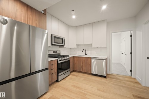 Modern kitchen featuring stainless steel appliances, two-tone cabinetry with light and wood-finish doors, a white subway tile backsplash, and light wood-finish flooring - 12171 177 Avenue, Edmonton, AB 