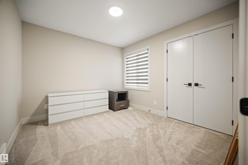 Plush neutral-toned carpeting enhances this bright room, featuring a double-door closet with modern black hardware, a window with horizontal blinds, and a recessed ceiling light fixture - 12171 177 Avenue, Edmonton, AB 