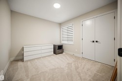 Plush neutral-toned carpeting enhances this bright room, featuring a double-door closet with modern black hardware, a window with horizontal blinds, and a recessed ceiling light fixture - 