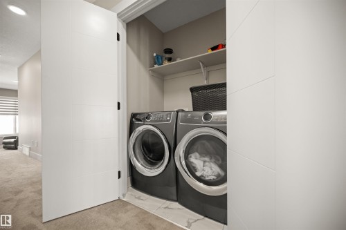 Dedicated laundry closet featuring a front-loading washer and dryer, integrated shelving, and a tiled floor - 12171 177 Avenue, Edmonton, AB 