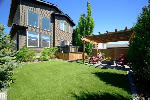 Expansive backyard featuring a lush green lawn, a wooden pergola over a paver patio with a built-in fire pit, and a raised wooden deck - 12171 177 Avenue, Edmonton, AB 