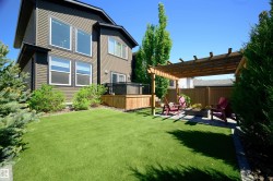 Expansive backyard featuring a lush green lawn, a wooden pergola over a paver patio with a built-in fire pit, and a raised wooden deck - 