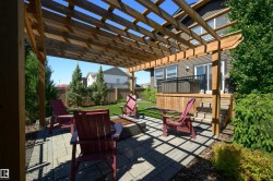 Expansive outdoor patio with a wooden pergola, paver stone hardscaping, built-in fire pit, and a manicured lawn - 