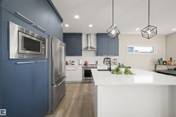 Contemporary kitchen featuring a large central island with a white countertop, two geometric pendant lights, stainless steel appliances, and two-tone cabinetry with blue and white finishes - 