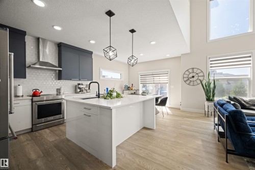 Modern kitchen featuring a white center island with an undermount sink, stainless steel appliances, dark cabinetry, and wood-finish flooring - 12171 177 Avenue, Edmonton, AB 