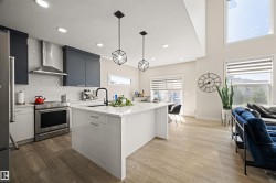 Modern kitchen featuring a white center island with an undermount sink, stainless steel appliances, dark cabinetry, and wood-finish flooring - 